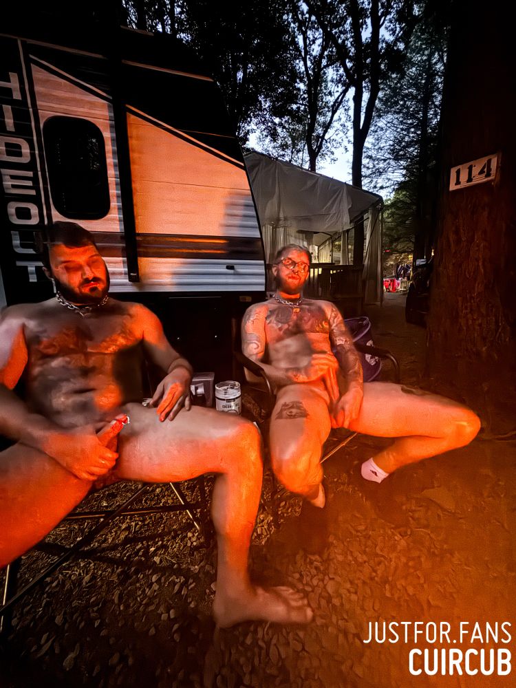 A photo of cuircub and siucra sitting in front of a camper on camp chairs, completely naked and glistening from coconut oil and the fir in front of them while they stroke their hard cocks.