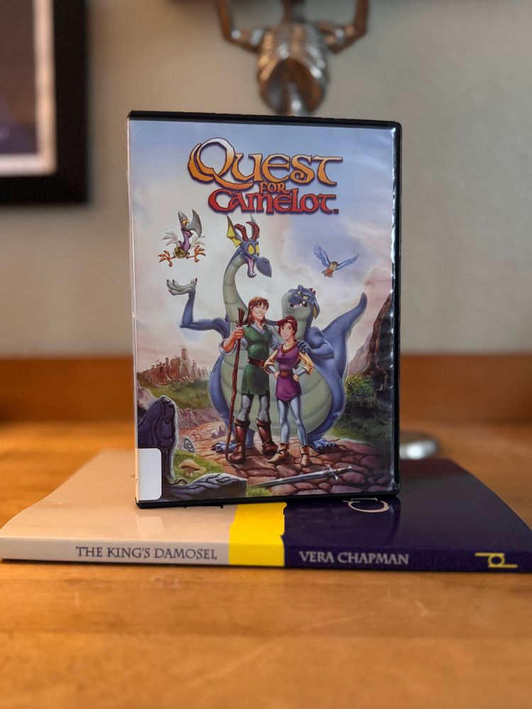 The DVD case for the 1998 animated film Quest for Camelot, sitting upright on top of the book The King's Damosel by Vera Chapman
