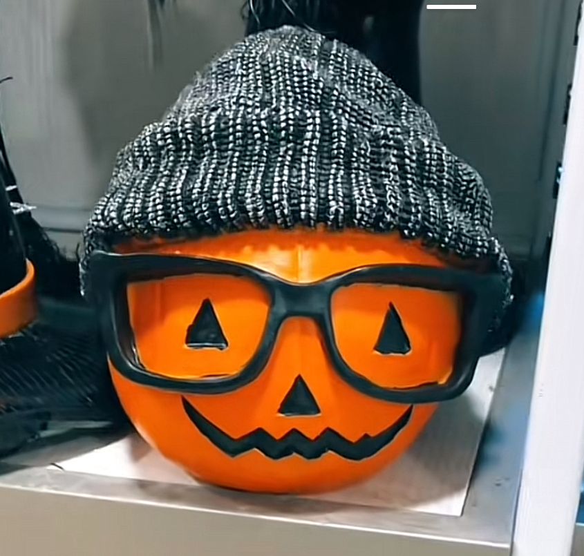 Foto de uma abóbora de halloween (com rosto feliz) usando um óculos de grau sem lentes preto e touca cinza