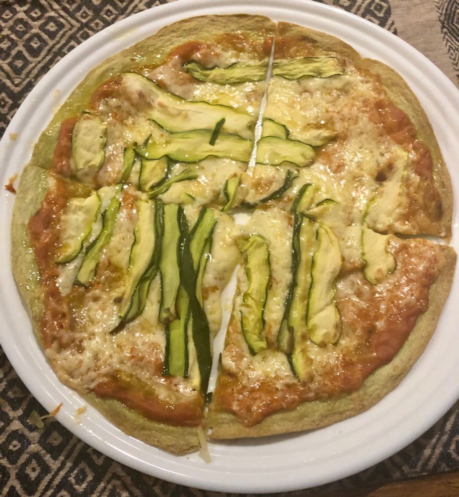 Flatbread topped with tomato sauce, cheese, and zucchini ribbons, tossed in the oven to make pizza. White plate, black and white placemat, nasty photo lighting