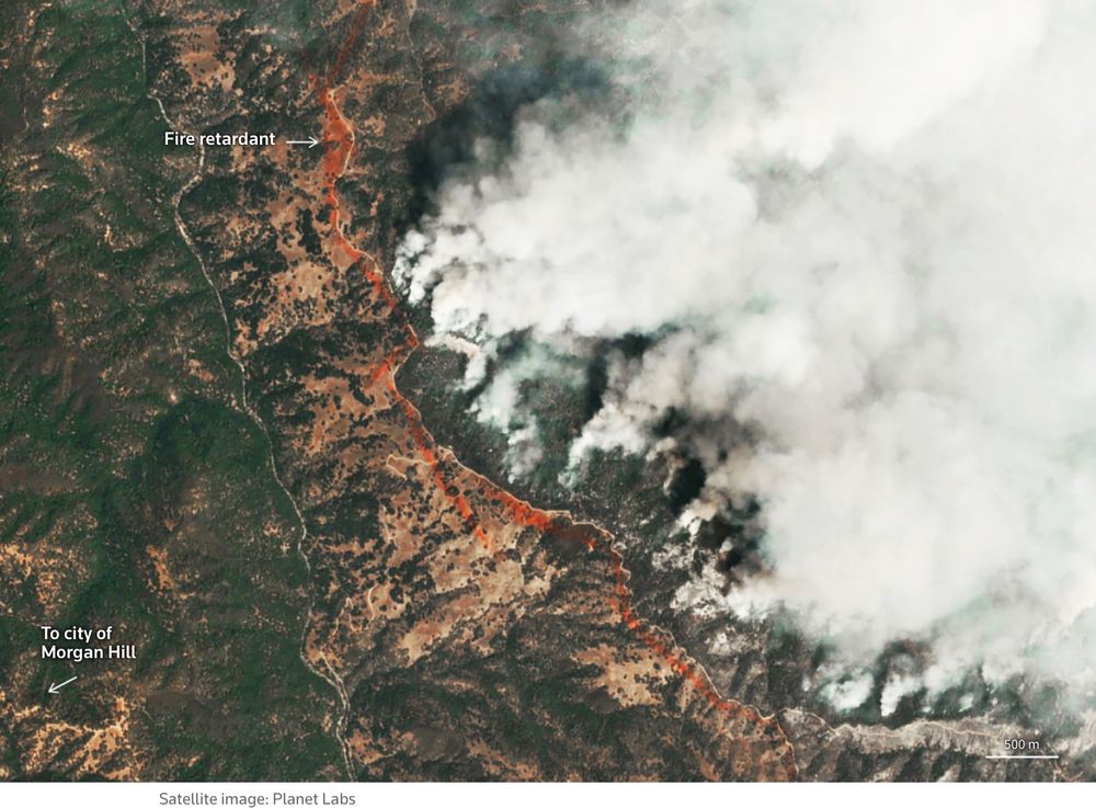 High-resolution color satellite image showing red flame retardant laid in front of an advancing fire with copious smoke.