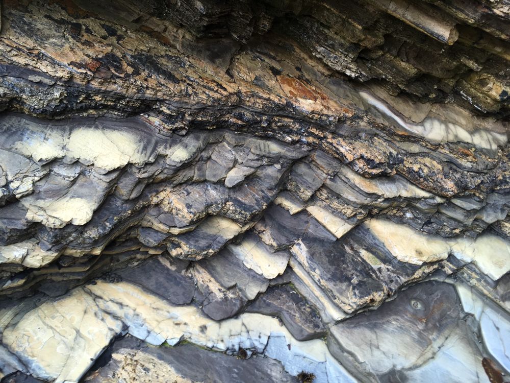 Rough layers of rock angling down toward the cave floor. The colors are dark to light gray, rust and light blue.
