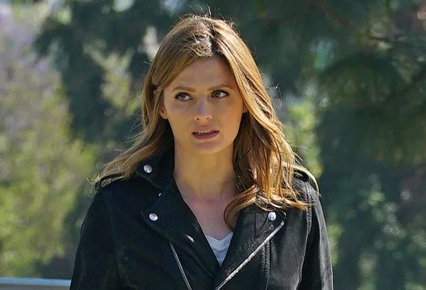 Stana Katic stands outside, wearing a black jacket over a white t-shirt.
