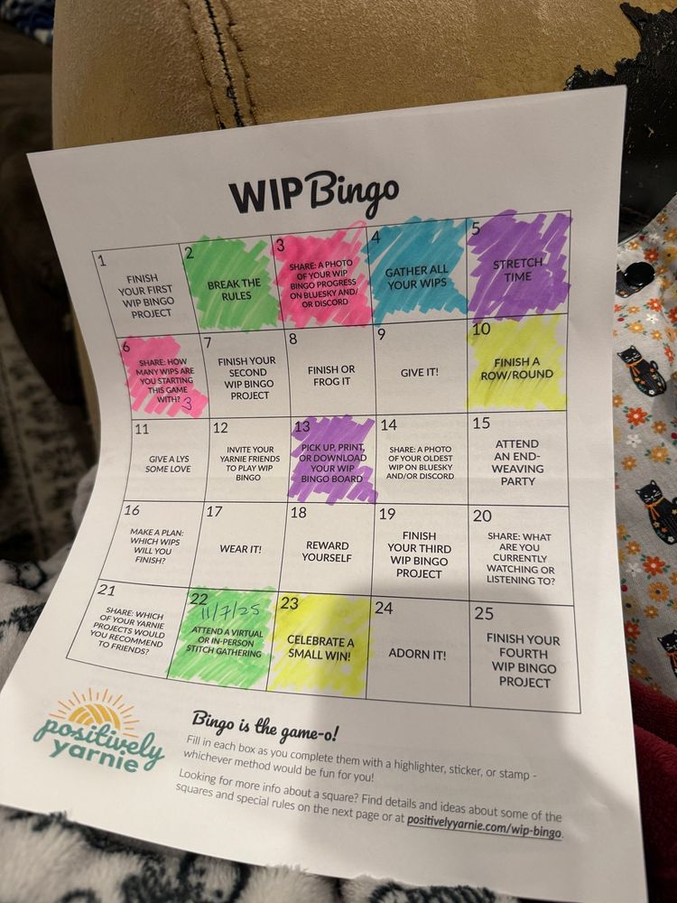 A piece of white paper with the WIP Bingo Card on it is propped against project bags. Nine of the squares are colored in in pink, blue, green, yellow, and purple highlighter. 