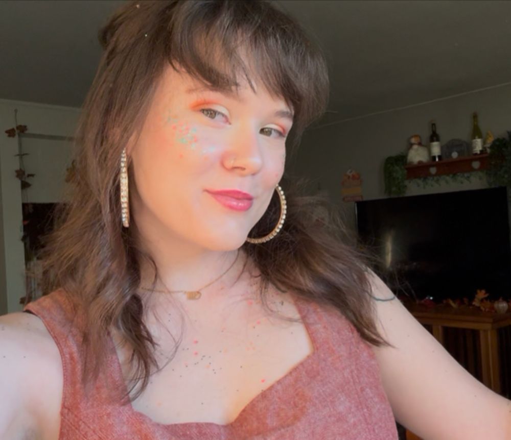 Selfie of me with showgirl glitter, smiling with sparkly hoops