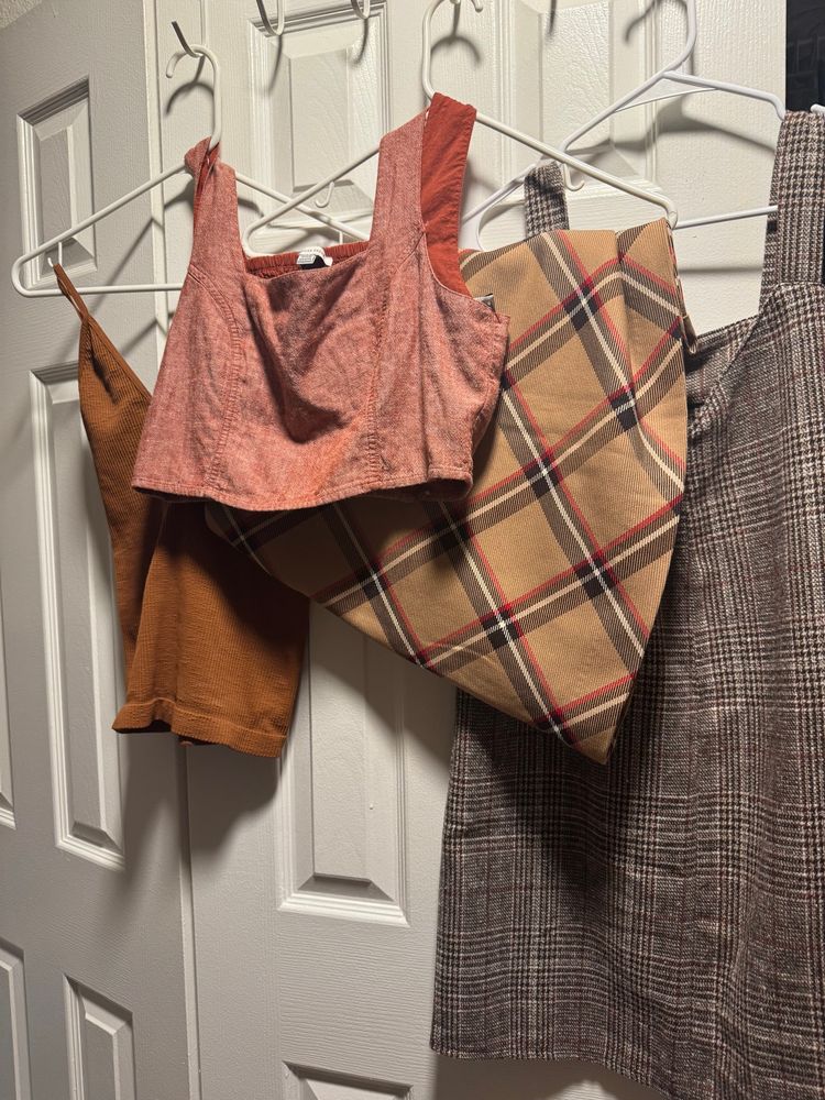 Clothes hanging up to take a picture; orange tops and plaid skirt and dress