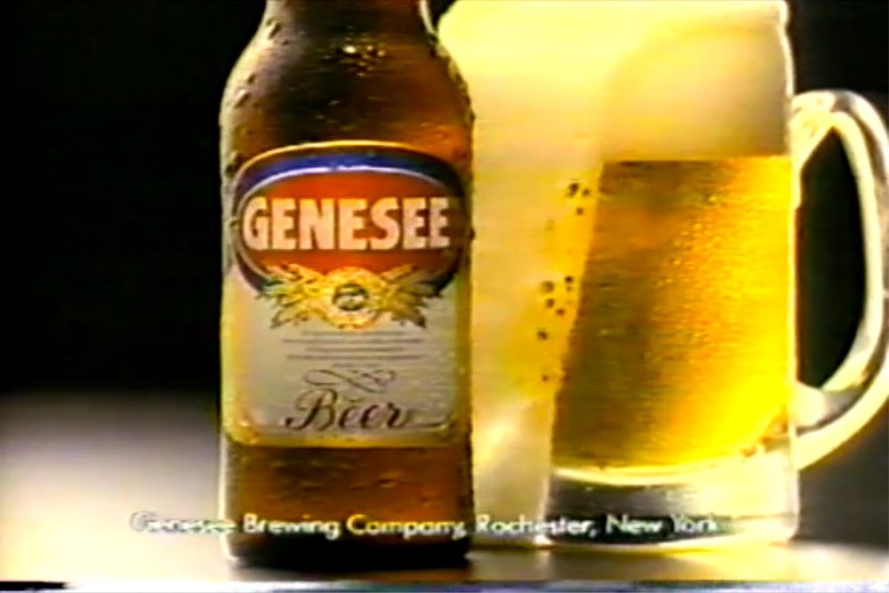 It's a bottle of Genesee beer next to a mug of Genesee beer that is perfectly foaming over and golden.