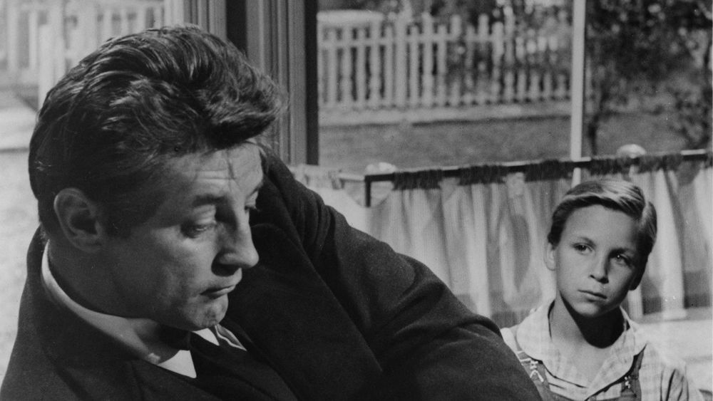 A still image in black and white of a man and a boy in front of a window. Night of the Hunter (1955)