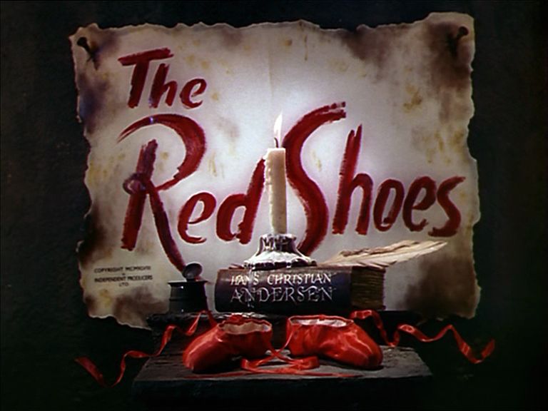 A candle on top of a book that reads Hans Christian Anderson with a pair of ballet slippers underneath. The title reads The Red Shoes. 