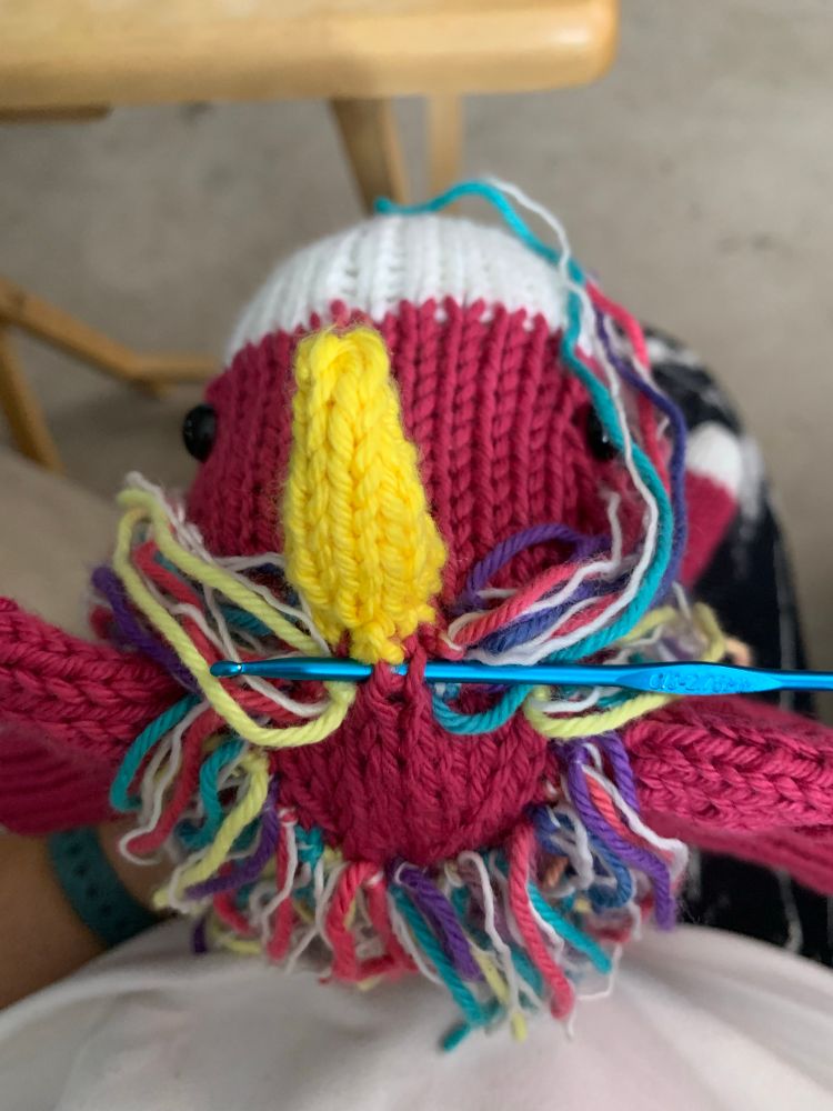 The top of a pink knitted unicorn in the middle of the mane being installed. 