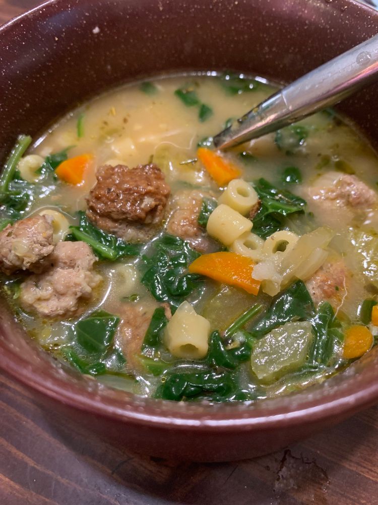 A closeup of a bowl of Italian wedding soup with meatballs, small pasta, carrots, celery, and spinach in a chicken broth. 