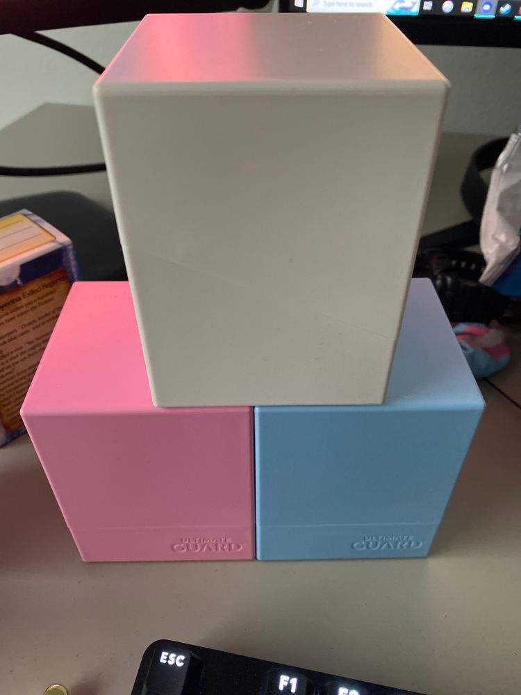 A pink and blue card deck box with a white box stacked on top