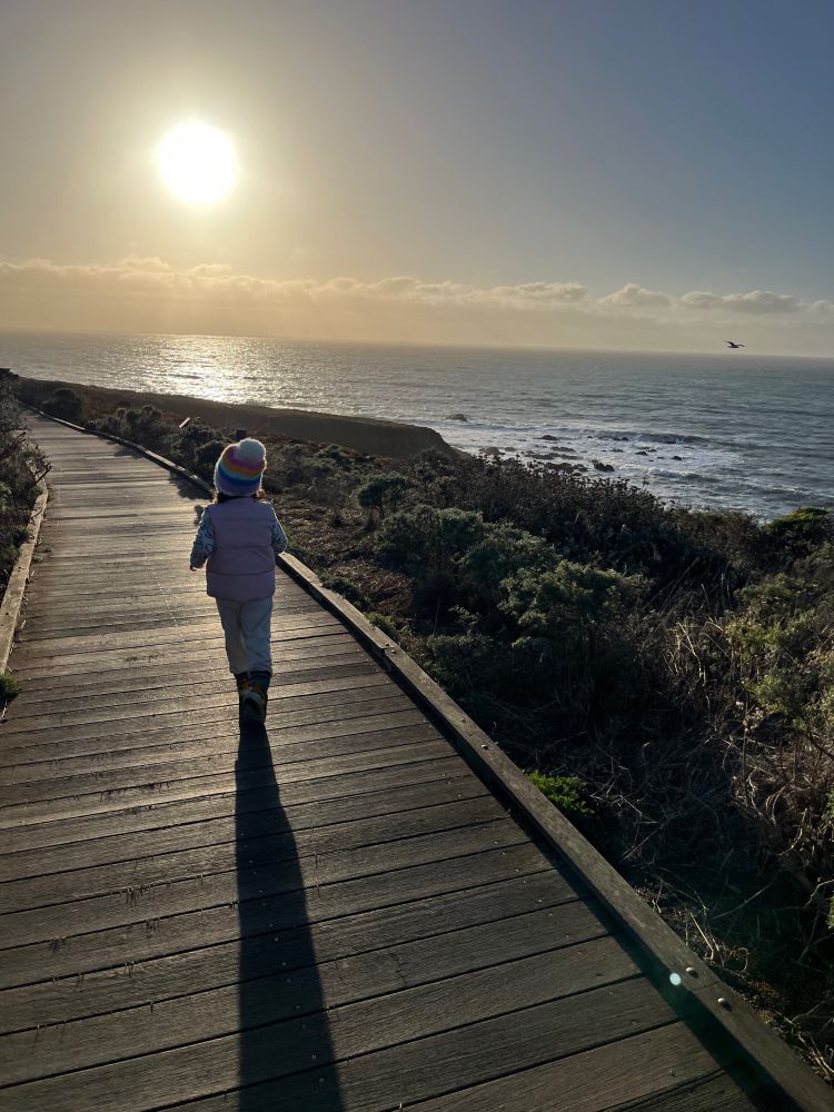 Kid running along hiking trail with ocean and sun setting in the background