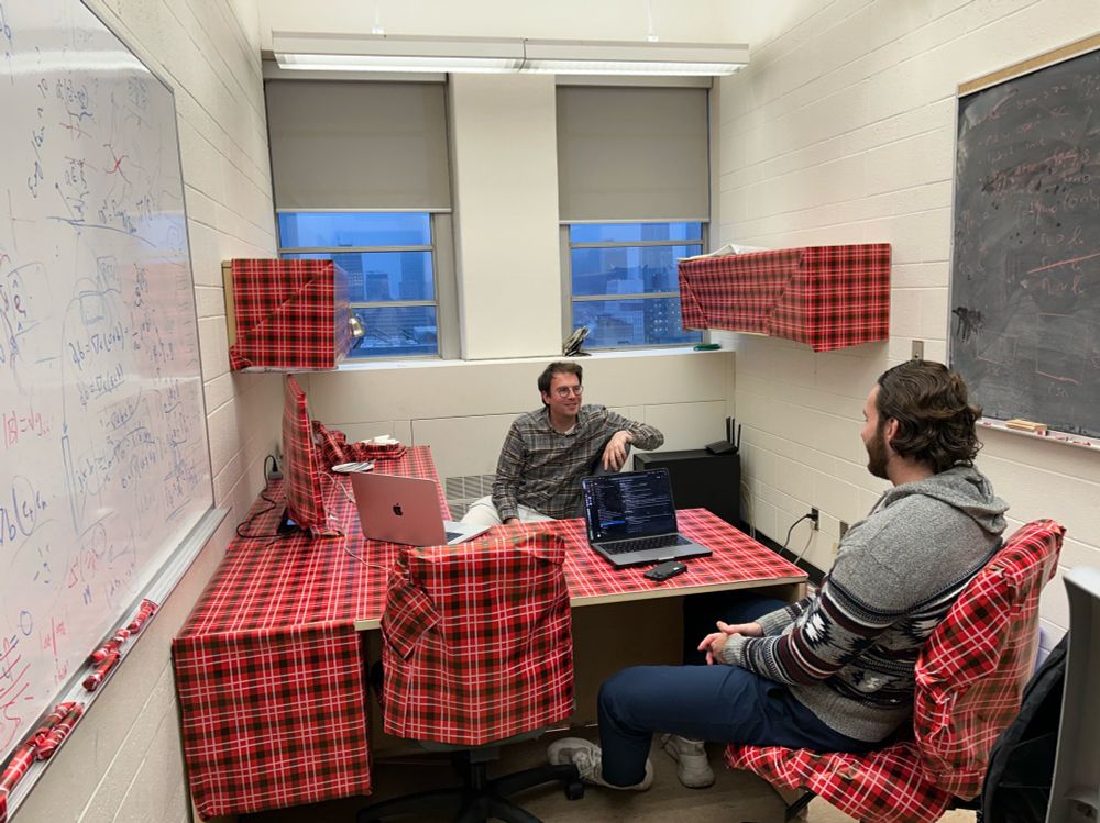 An academic meeting a student in their office. But half of their office is wrapped in Christmas wrapping paper.