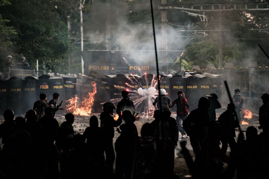 a group of protesters surround a line of police wielding riot shields 