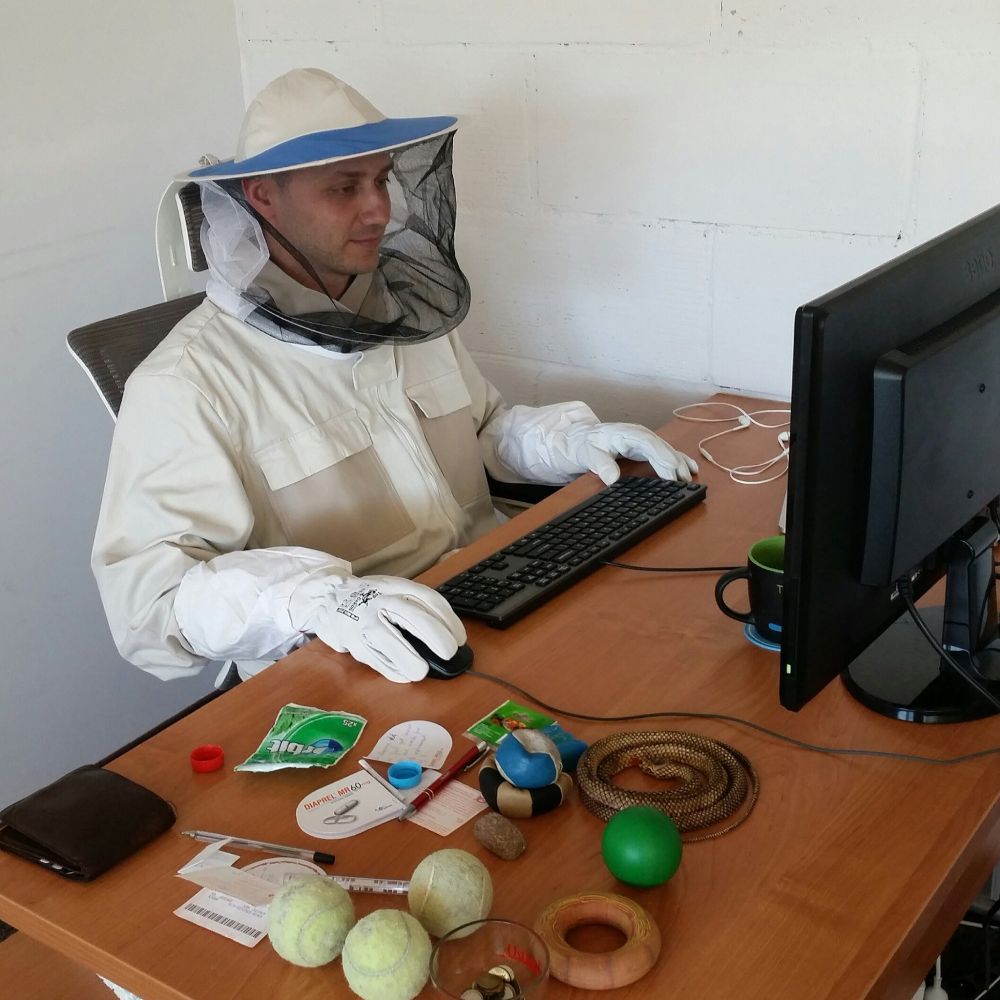 An extremely handsome software developer is pretending to work wearing a beekeeper's outfit.