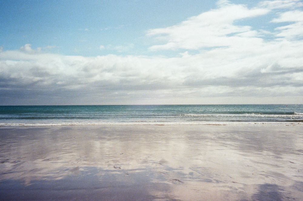 Beach with wet reflective sand and blue sky and white clouds above 