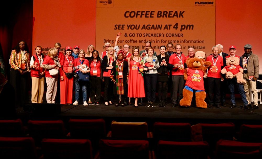Group of individuals standing on stage at a Rotary International event with many wearing red "End Polio Now tshirts and holding plush bears.