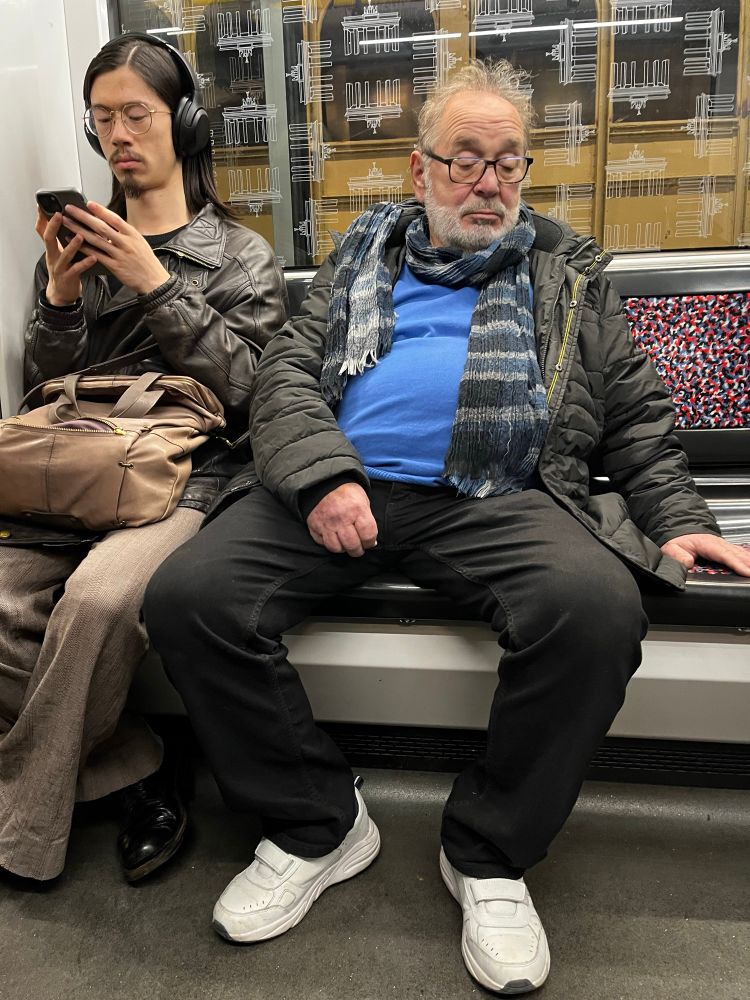 En yngre man i en tunnelbanevagn i Berlin som kläms in i hörnet av en äldre man med ett rejält manspread. 