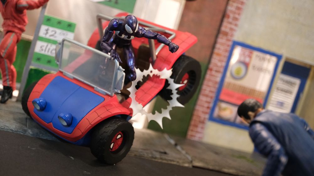 Ultimate Spider-Man in his black suit is behind the wheel of the Spider-Buggy, but is hit by Hammerhead and is careening into a pizzaria window.