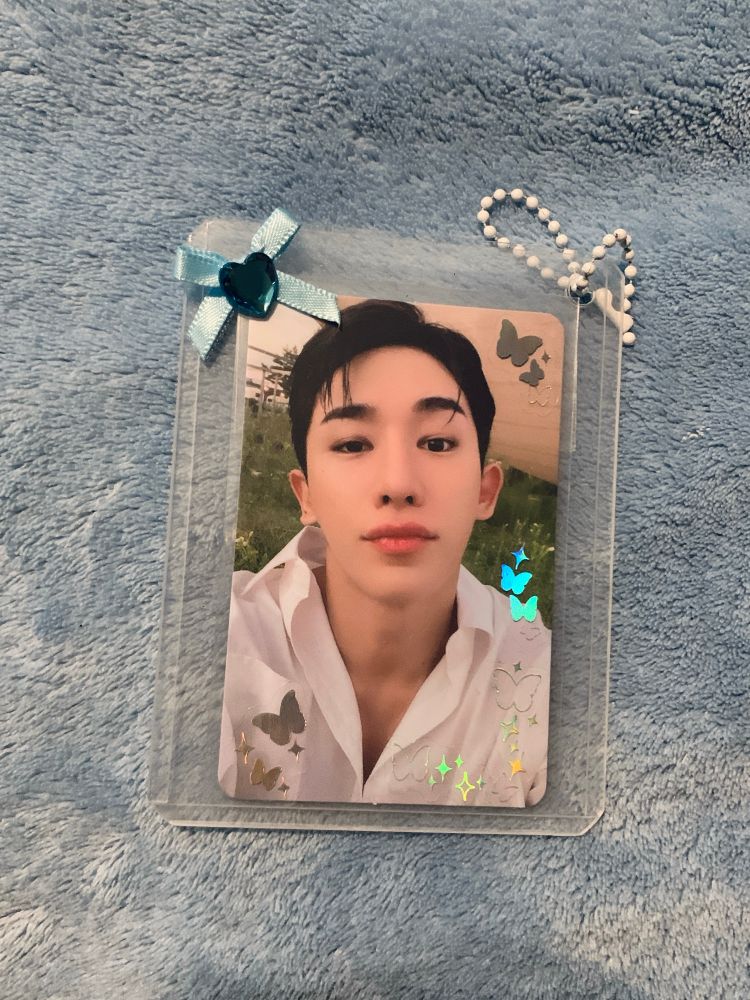 A photocard of Wonho inside a hard photocard sleeve with small butterfly stickers and a blue bow 
