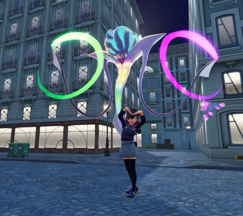 Anizée, now dressed in a way that looks more like Malamar with her hair down, red accents now dyed purple, a Malamar-like shirt, a light grey skirt, and black thigh-highs, is making a heart with her arms, looking very happy, while the Alpha Mega Malamar stands behind her.