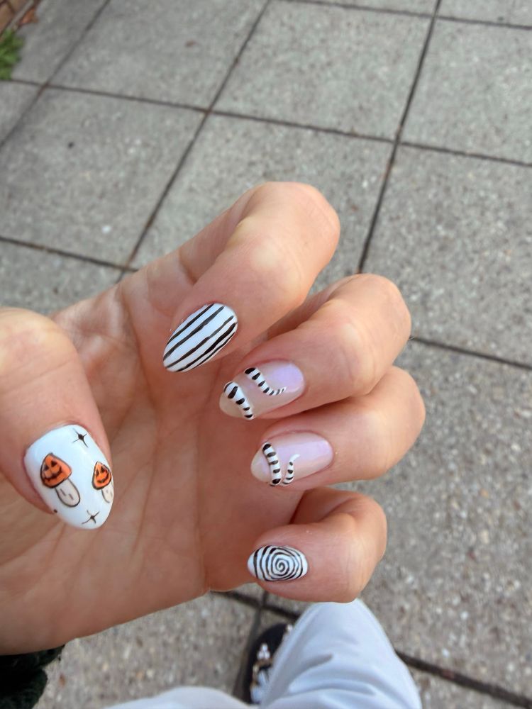 Picture of my nails with jack o lantern mushrooms on my thumb and black and white striped nails inspired by the snake worm from Beetlejuice