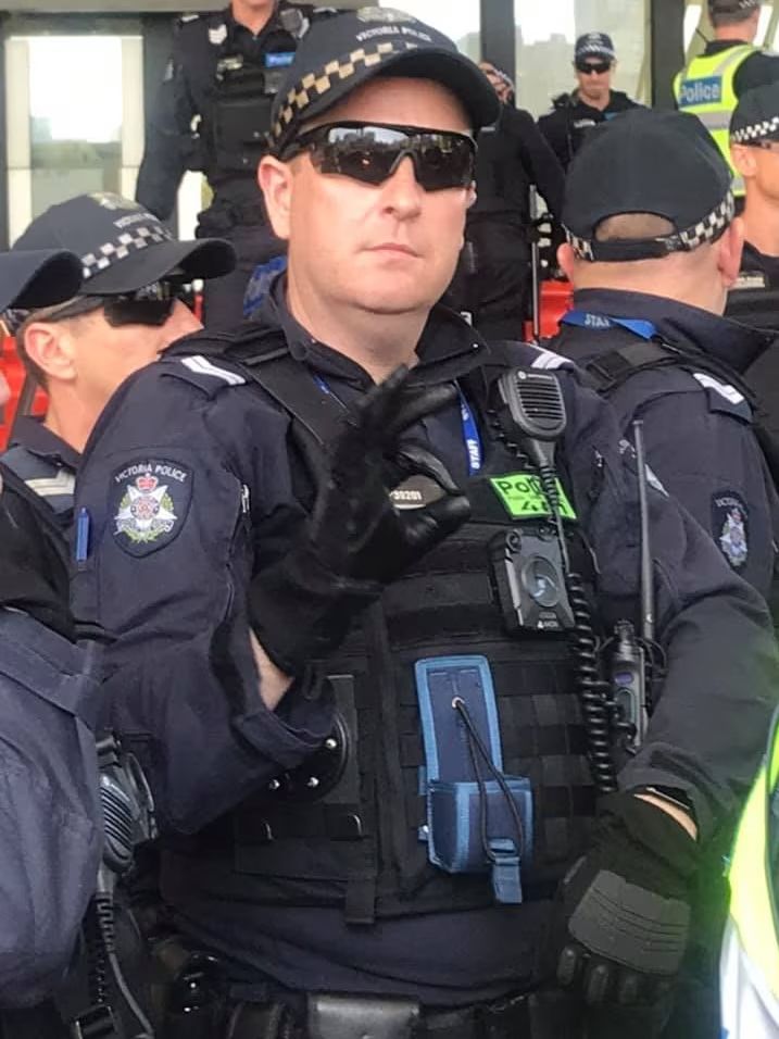 a uniformed police officer displaying a known white supremacist hand gesture.