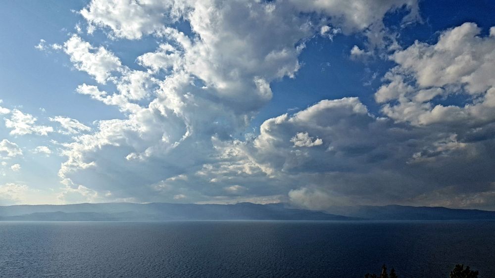 Mixed clouds over Flathead lake, beams of sunlight shining down, dark mountains across the lake