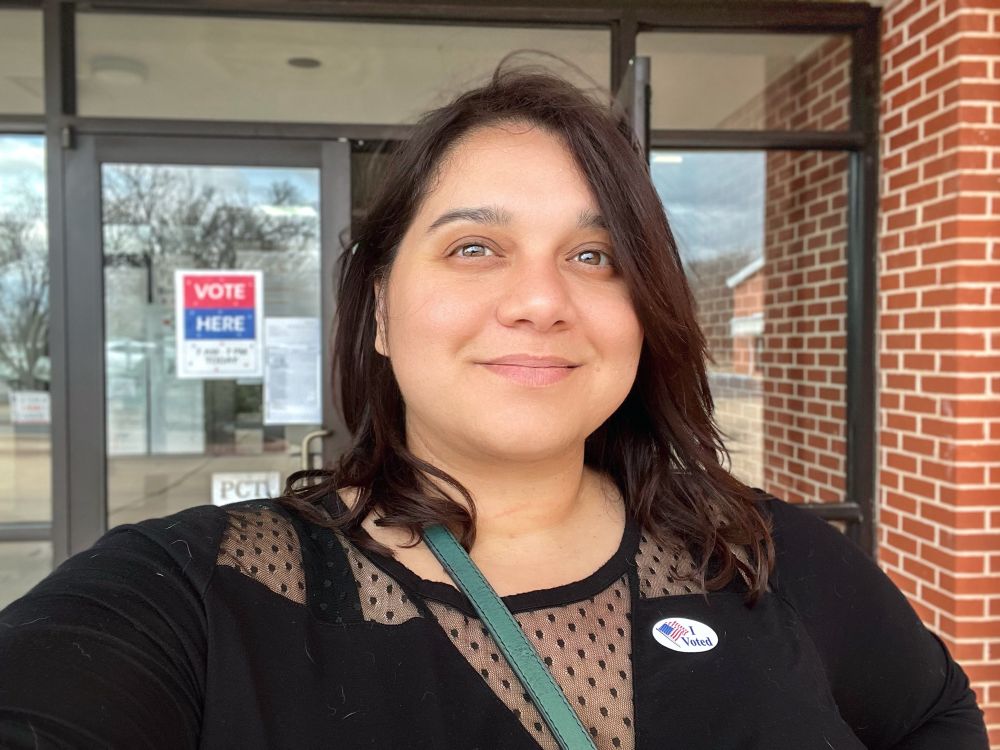 Helen Grant stands outside polling station wearing a “I voted” sticker