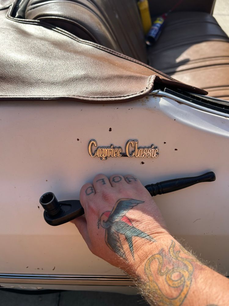My tattooed hand holding a ratchet under the emblem of my Caprice Classic. The convertible top is down and covered by the boot. 