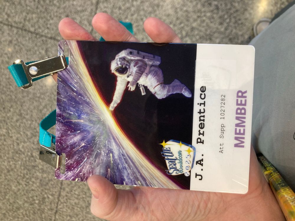 Worldcon badge with my name on it. Illustration of an astronaut touching a kaleidoscopic curve of light