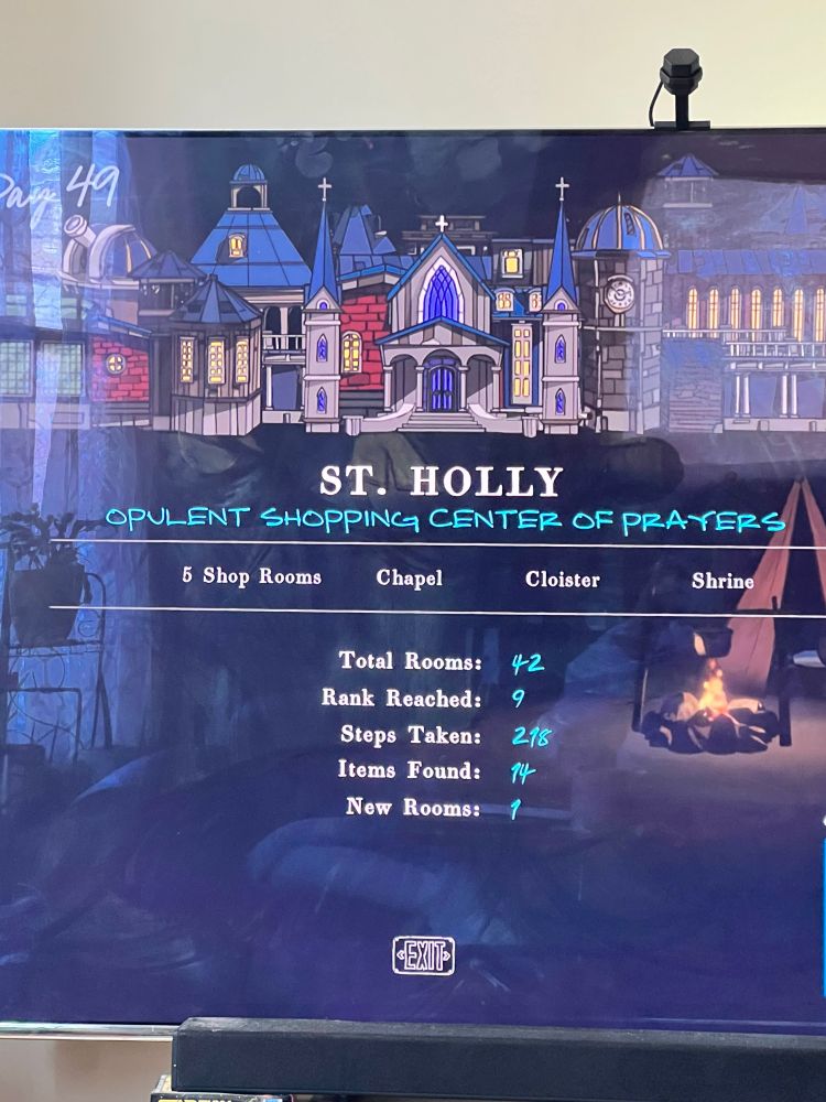 The same End Of Day screen as described in the previous image alt text. On this day the name of Mt. Holly was changed to St. Holly, and the description is “Opulent Shopping Center of Prayers.” The rooms that earned the title include having 5 shops, the chapel, the cloister, and the shrine. Additional details from the day were Total Rooms: 42, Rank Reached: 9, Steps Taken: 218, Items Found: 14, and New Rooms: 1.
