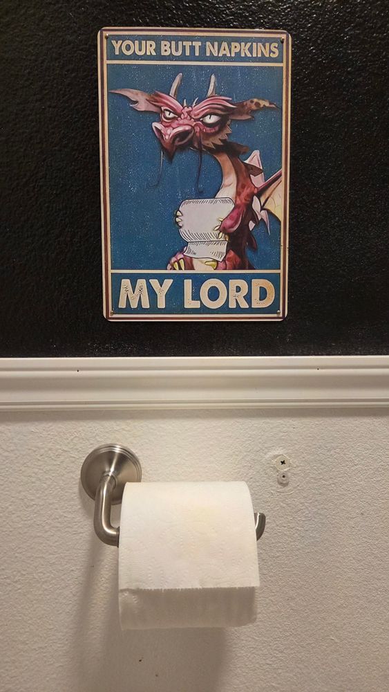 A photo of a roll of toilet tissue with a painted sign over it. the painting features a small dragon holding a roll and is captioned "YOUR BUTT NAPKINS MY LORD."