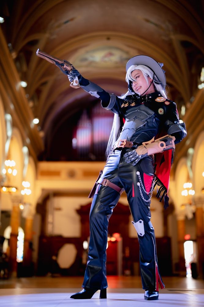 a fullbody photo of connie cosplaying Boothill from Honkai: Star Rail. They are looking to the left while aiming with a revolver. The background is a church with an organ and arched ceiling.