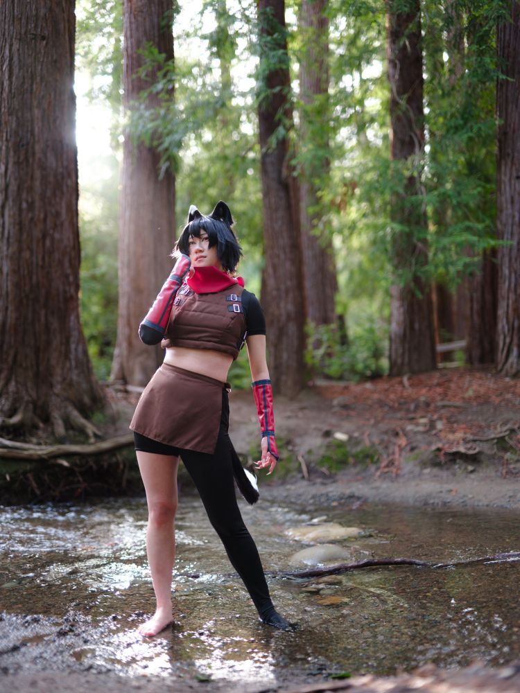a photo of connie cosplaying Izutsumi from Dungeon Meshi. they are standing in a river with tall redwood trees behind them. they are looking into the camera with one hand adjusting their scarf.