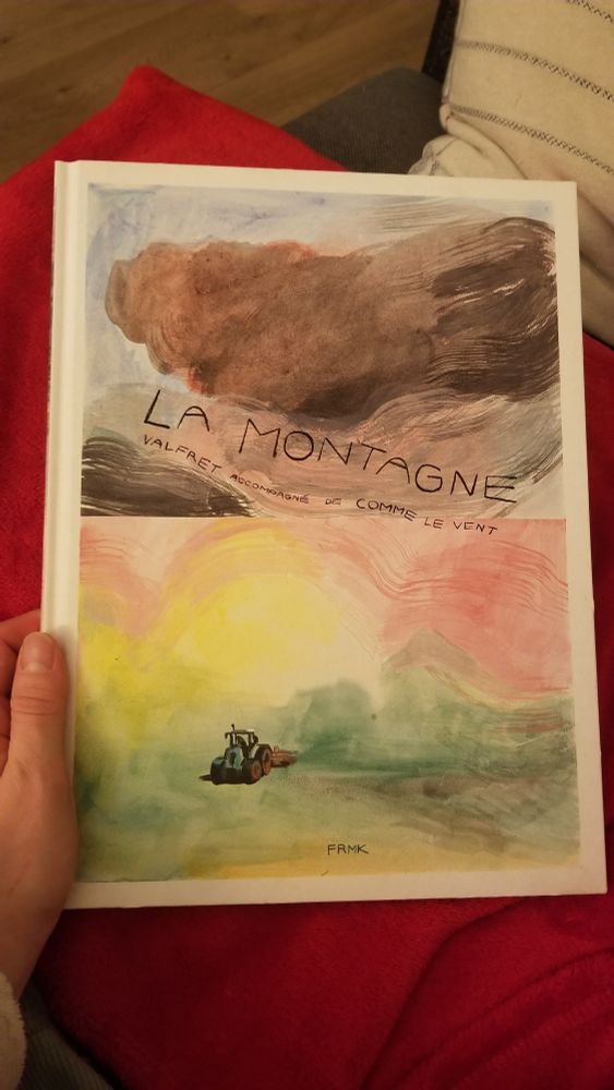 Photo du livre fermé dans ma main, la 1ere de couverture montre un paysage de campagne presque abstrait avec de gros nuages gris et un tout petit tracteur