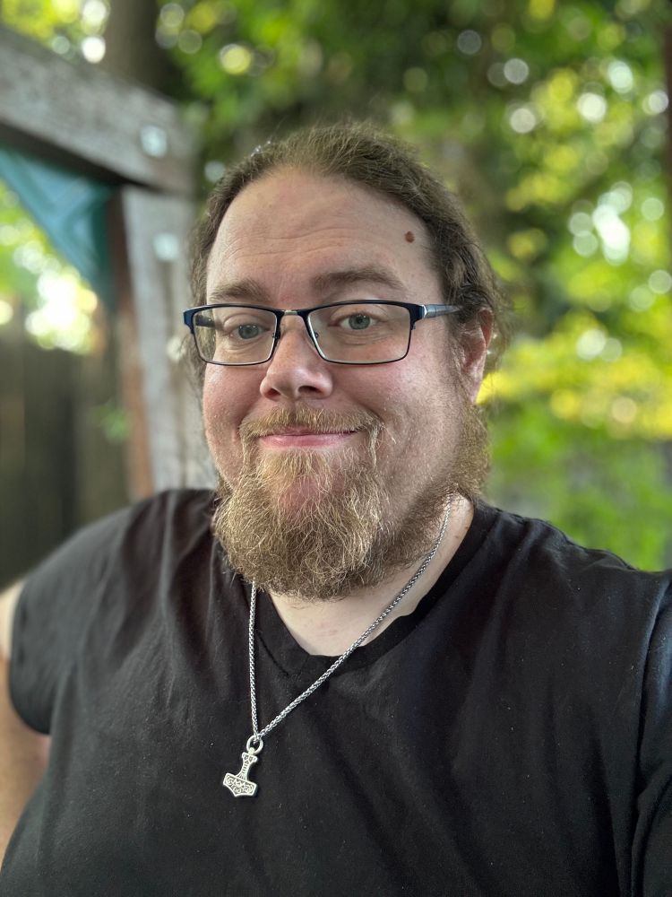 A bearded white guy in glasses wearing a black t-shirt and a silver Thor’s Hammer necklace. He seems okay, I guess. I mean I like him. Maybe you would like him too, if you met him.