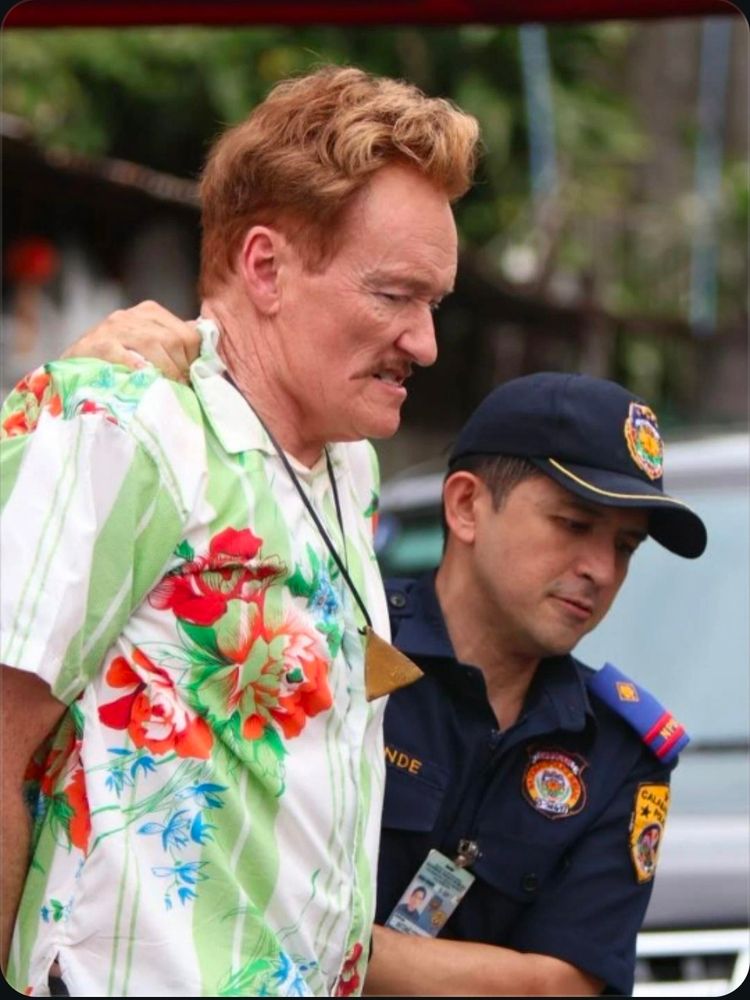 A cop arresting a tall man with red hair and a mustache in a Hawaiian shirt