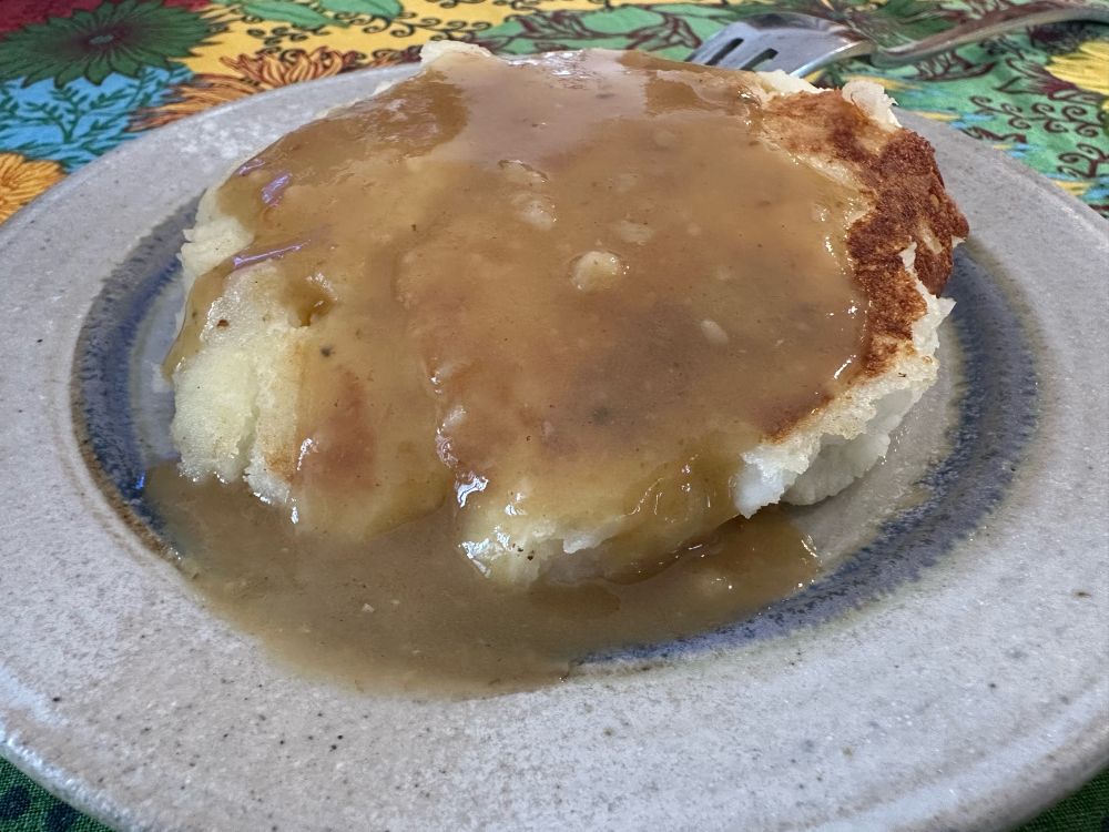 A gravy-covered patty of fried mashed potatoes on a stoneware plate