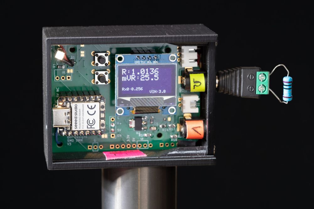 A small DMM in a printed housing, about 2x3x1" big, with a 1 Ohm resistor connected to resistance circuit.