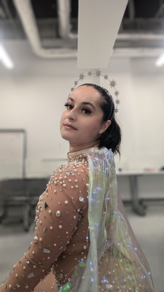 A brunette looking over her shoulder in a star crown, gemstone bodysuit and LED wings