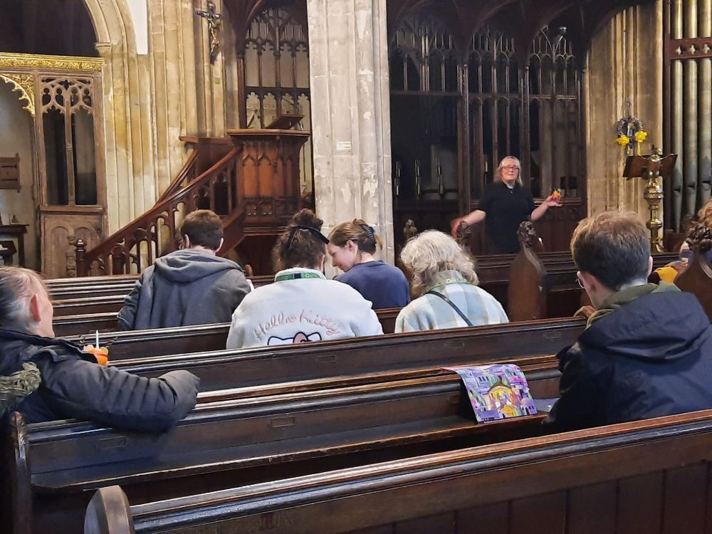 Lead Evangelist Hannah Seal stands at the front of church holding a Christingle. The congegation are shown from the back.