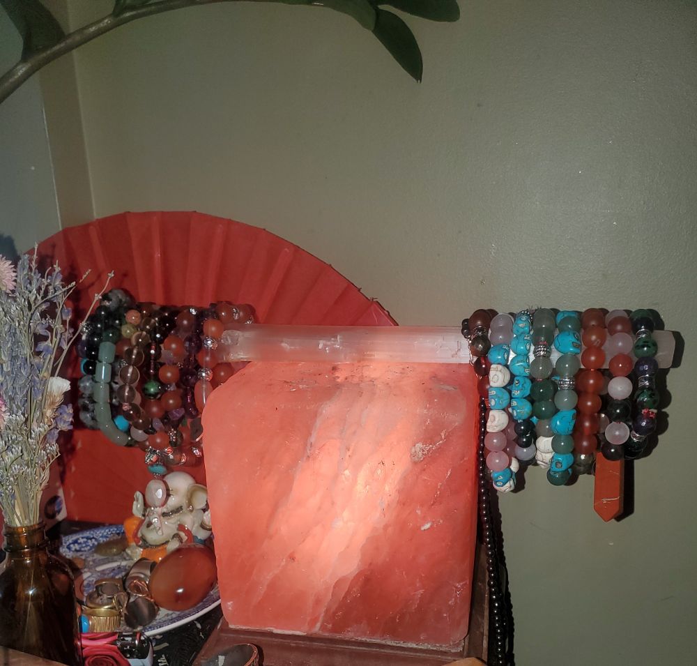 A beautiful square shaped Himalayan salt lamp with a selenite stick on top. The Selenite stick holds several crystal bracelets featuring Rose Quartz, Red Agate, Smoky Quartz etc