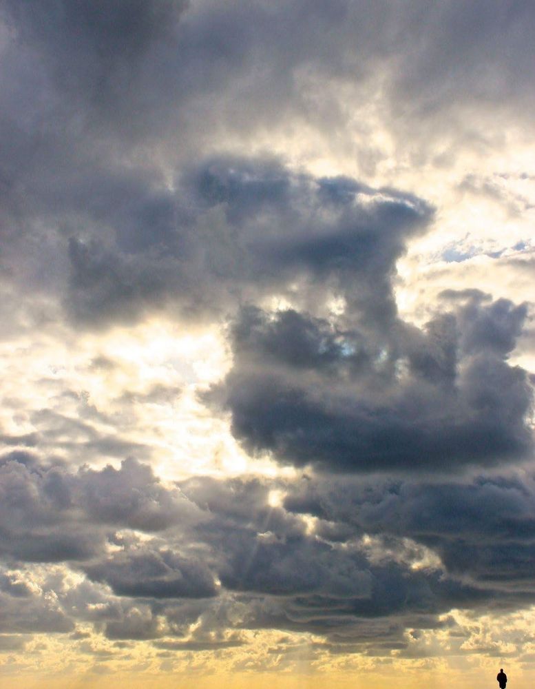 Photograph of clouds stretching into the horizon with an extremely small silhouetted human in the bottom right corner 