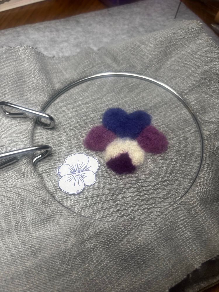 A felted pansy in off white and purples alongside a smaller paper pansy