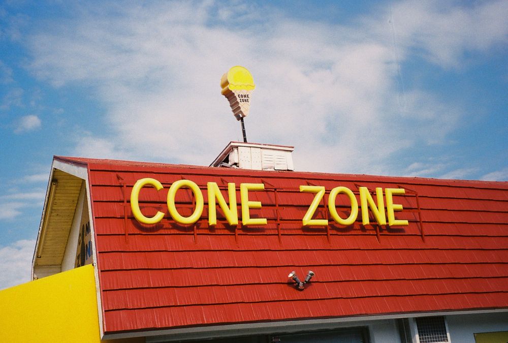 A photograph of an ice cream shop with signs that say CONE ZONE in big yellow letters against a red shingled roof