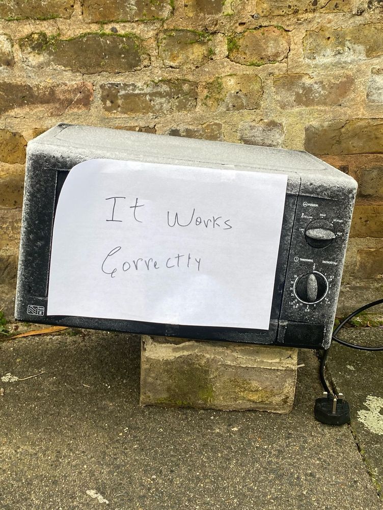 A discarded microwave covered in frost with a handwritten sign saying ‘it works correctly’