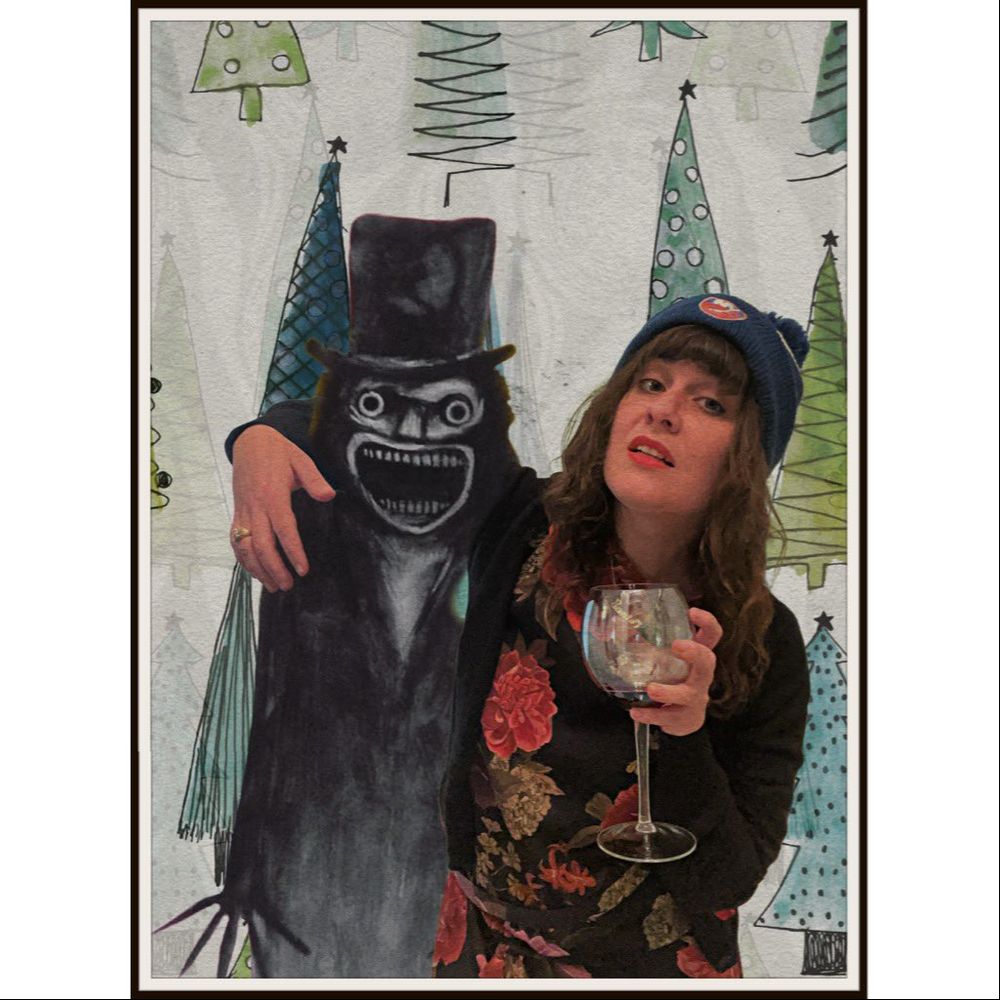 Photo of a woman with her arm around the babadook and the other hand holding a glass of wine, backdrop is christmas trees