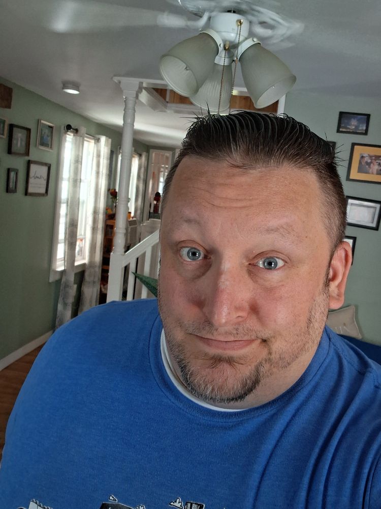 A middle aged man with short brown hair smiling in a blue shirt. 